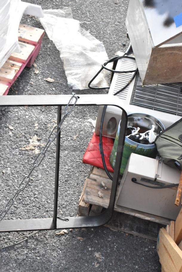 Black metal pot rack with hanging chains, in used condition, lying on pallets outdoors.