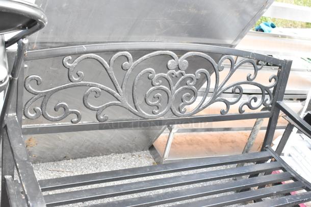 Black metal bench with armrests, features intricate scrollwork design. Good condition; durable and elegant for outdoor use.