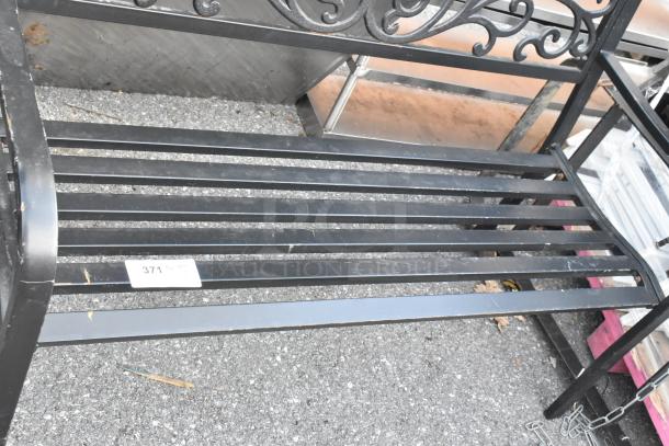 Black metal bench with armrests, decorative backrest, and slatted seat. Moderate wear visible. Tag marked "371."