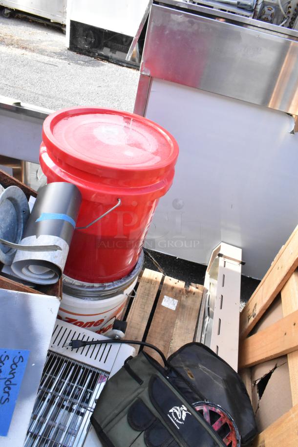 Pallet with mixed items including a red plastic bucket, metal tubing, a bag, and scattered equipment, all in used condition.