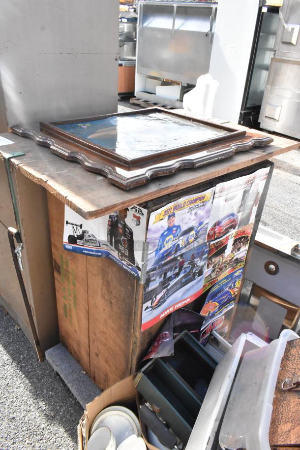 Rustic wooden table with scalloped edges and a reflective tabletop panel. Various items and posters are placed around it.