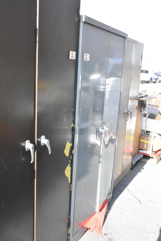 Three various 2-door cabinets with numbered labels 1, 2. Black and grey, showing wear. Auction item multiplying value.