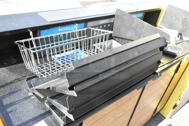 Wooden counter with four doors, features a metal recycling bin and black plastic trays on top, in used condition.