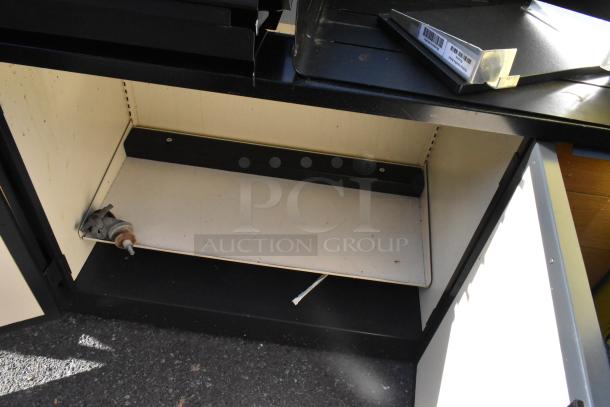 Wooden counter with four doors, shelves inside, and metal contents. Moderate wear, suitable for storage or display use.