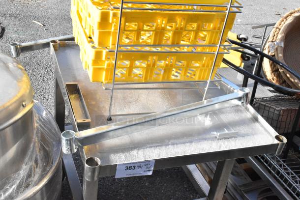 Stainless steel table on commercial casters, surface with assorted contents including yellow plastic crates, in used condition.