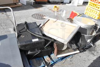 Pallet lot of miscellaneous items including black boxes, metal container, wood panel, and plastic crates. Condition varies.