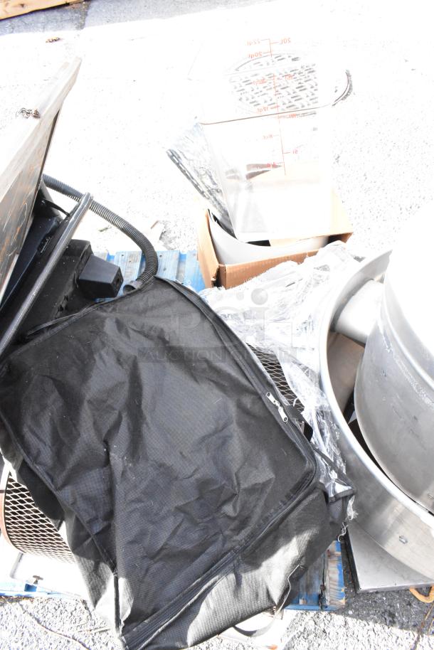 Pallet lot of assorted items including a black bag, clear container with measurement markings, metal drums, and various boxes.