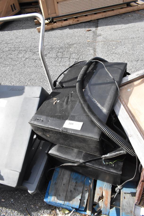 Pallet of various items including black padded equipment with labels, metal furniture frame, and wooden pallets, in used condition.