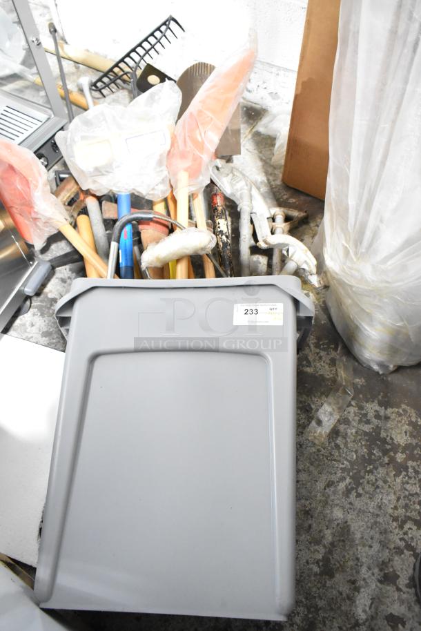 Gray Slim Jim trash can containing various tools, including a rake, broom, and shovel; lot number 233 visible.