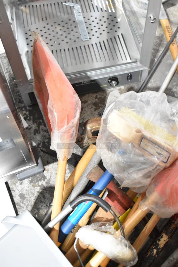 Gray Slim Jim trash can containing various tools: rake, broom, shovel. Tools appear in used condition with protective plastic covers.