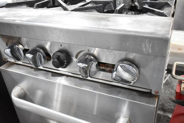 Stainless steel commercial gas-powered 4 burner range with oven, visible knobs, and sturdy handle, in used condition.