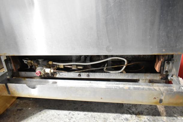 Stainless steel commercial gas-powered 4 burner range with oven base. Visible connection points and hardware. Used condition.