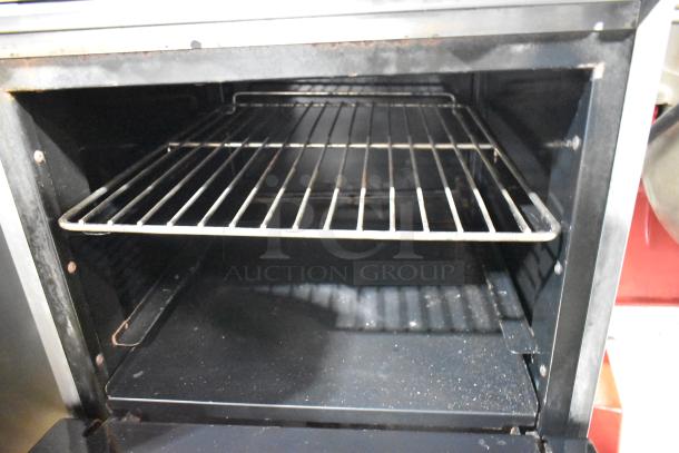 Stainless steel commercial gas-powered 4-burner range with oven; interior view showing oven rack. Clean condition.