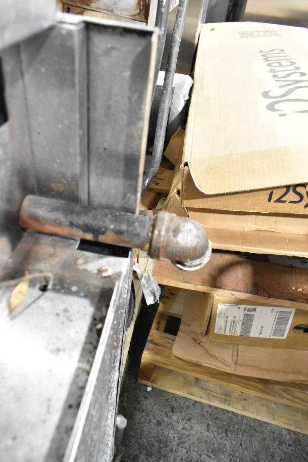 Stainless steel commercial gas-powered 4-burner range with oven, showing metal gas pipe and nearby cardboard boxes. Signs of use.