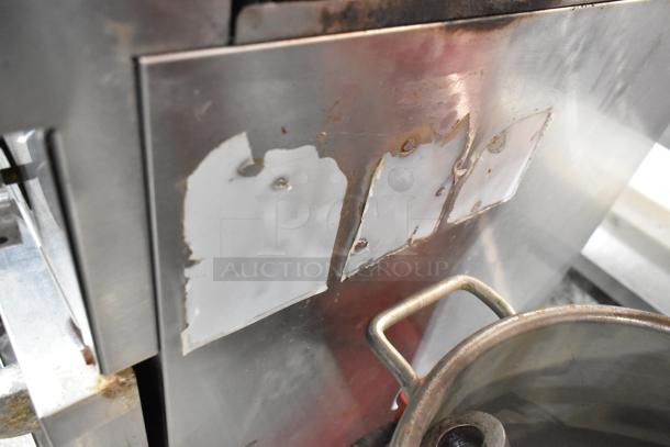 Stainless steel commercial gas range with four burners and oven, showing wear and missing labels, used condition.