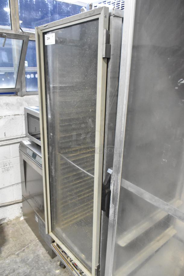 Omcan metal commercial heated holding cabinet on casters, large glass door, adjustable shelves, tag indicates model and serial number.