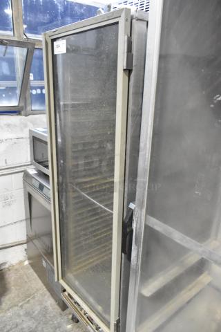 Omcan metal commercial heated holding cabinet on casters, large glass door, adjustable shelves, tag indicates model and serial number.