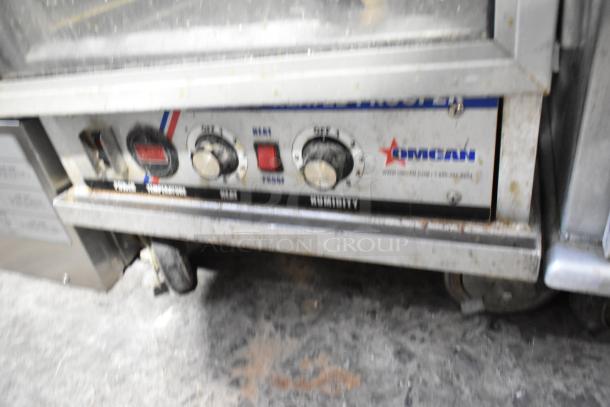 Omcan metal commercial heated holding cabinet with temperature and humidity controls, visible knobs, and Omcan logo on commercial casters.