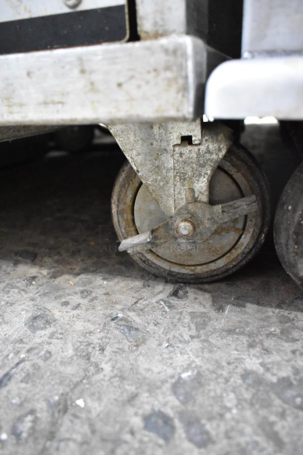 Omcan metal commercial heated holding cabinet on commercial casters, showing close-up of caster wheel, used condition.