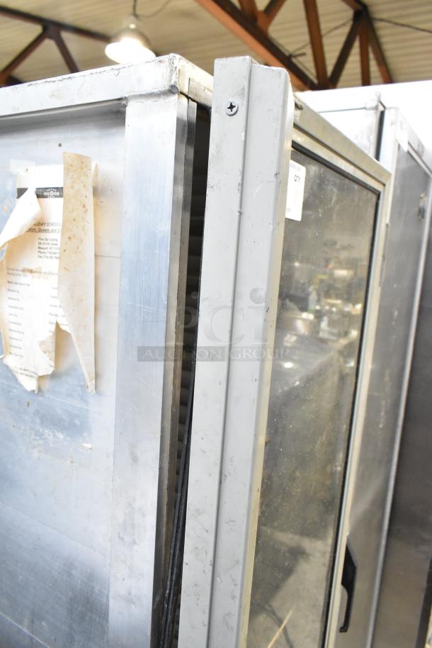 Omcan metal commercial heated holding cabinet with glass front door and commercial casters, showing signs of wear.