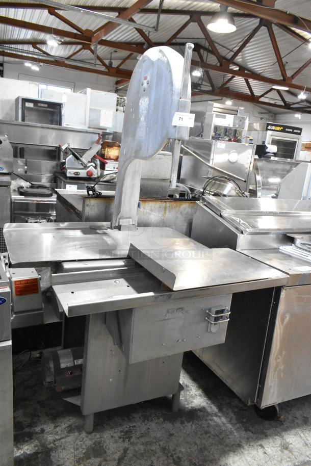 Metal commercial floor-style meat saw, industrial-grade, robust construction, visible wear on table and frame, electric motor.