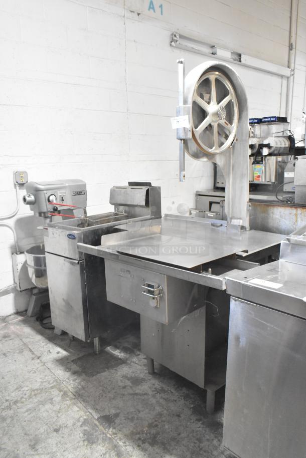 Metal commercial floor-style meat saw with large circular blade and stainless steel table, in used condition, ideal for heavy-duty cutting.