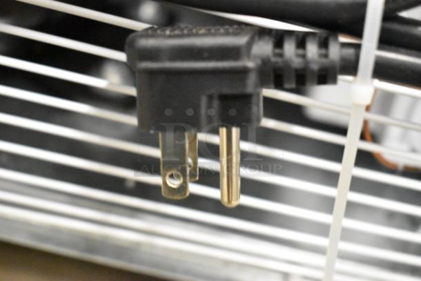 Close-up of the power plug for KoolMore KM-MDR-1GD-10C cooler, showing standard 115V plug and metal grid on background.