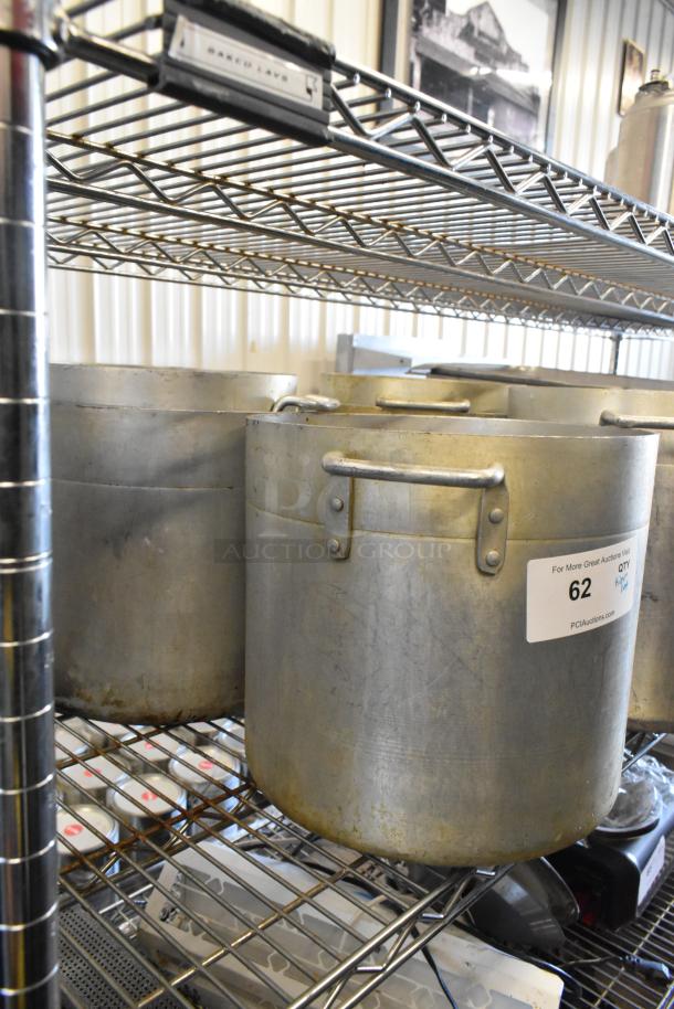 Metal stock pots on wire rack, showing signs of wear, includes stainless steel drop-in bins. Lot tagged as "62, QTY."