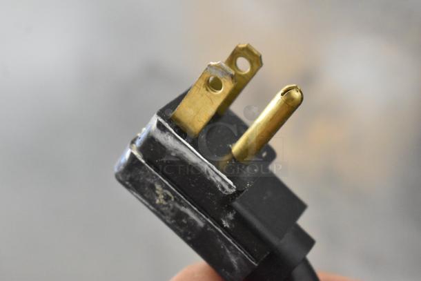 Close-up of a three-prong electrical plug, showing wear on metal prongs. Part of Traulsen RHT132WUT-FHS cooler.