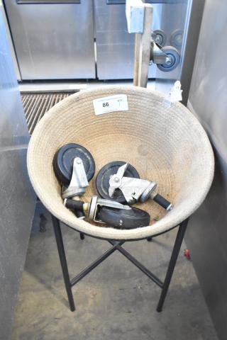 Basket on metal stand holding three commercial casters, showing auction tag "86." Durable, versatile storage unit.