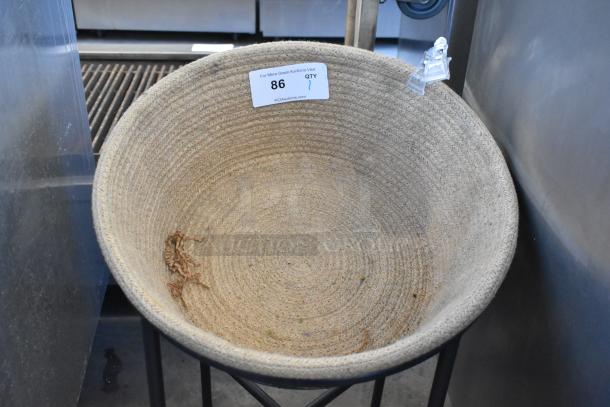 Woven basket on metal stand with three commercial casters, auction tag number 86 visible. Suitable for storage or decor.