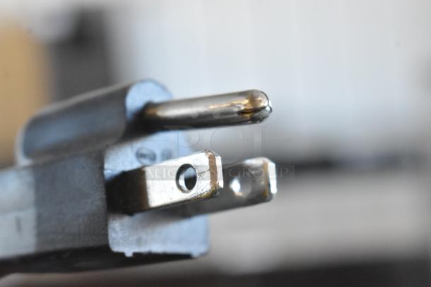 Close-up of a metal electrical plug with visible wear and a background suggesting an indoor setting.