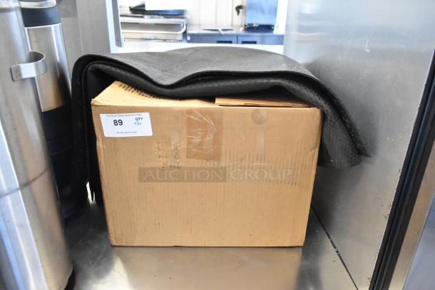 Cardboard box with paper bags, topped by a black rug. Auction label states, "For More Great Auctions Visit PCIauctions.com QTY x2."