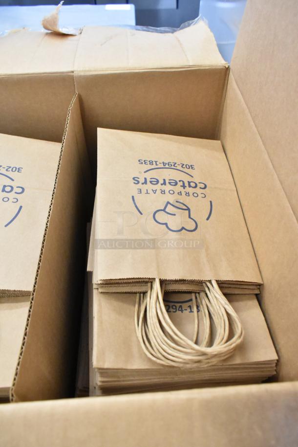 Box of paper bags with handles, labeled "Corporate Caterers" and "302-294-1835," indicating business use.