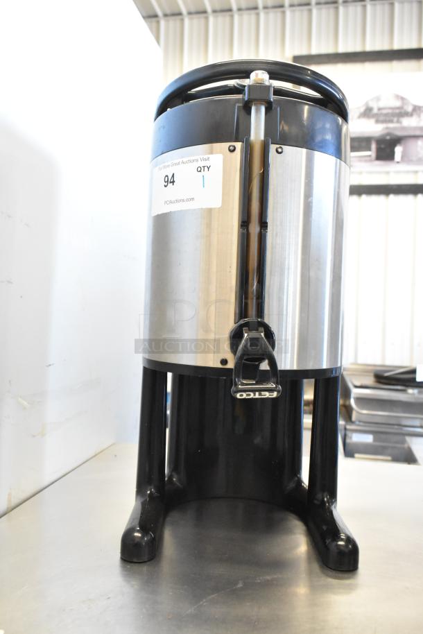 Fetco stainless steel beverage dispenser, used condition, with dispensing tap and sturdy black base. Auction tag visible.