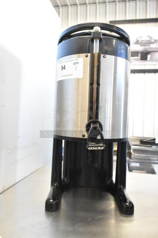 Fetco stainless steel beverage dispenser, used condition, with dispensing tap and sturdy black base. Auction tag visible.