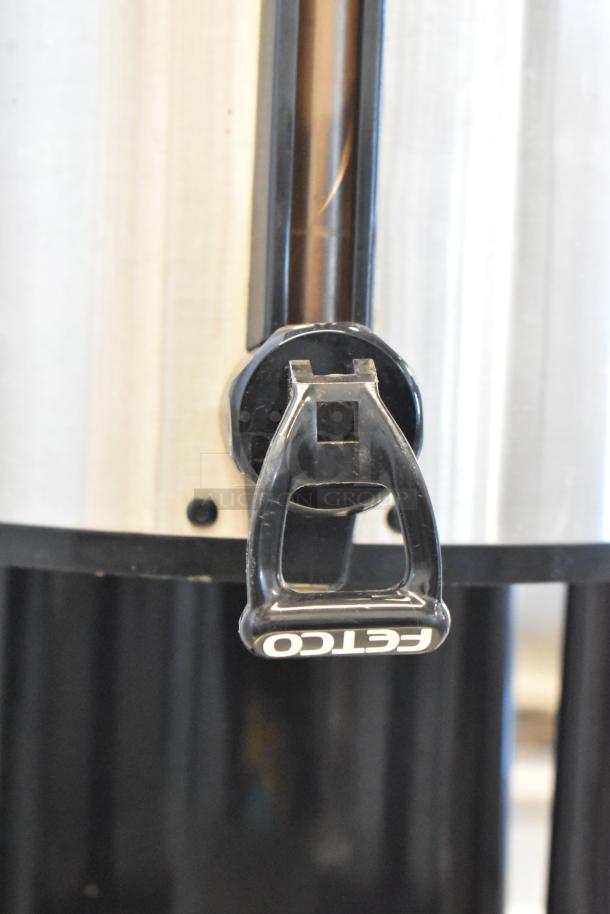 Fetco stainless steel beverage holder dispenser, black tap with Fetco branding, in good condition.