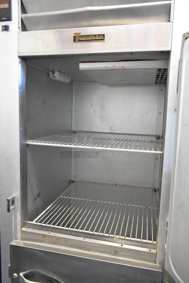 Traulsen G12000 stainless steel commercial freezer with two half-size doors. Features metal racks, visible Traulsen logo. Condition: Used.