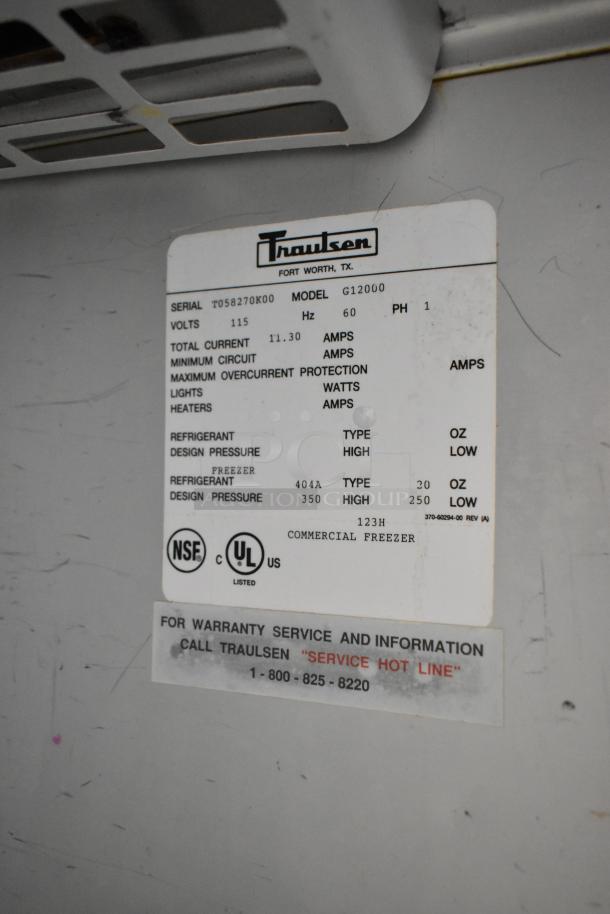 Traulsen G12000 stainless steel commercial freezer, 2 half doors, metal racks, 115V, 1 phase; label shows specs and contacts.