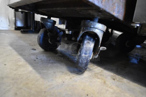 Southbend stainless steel 2-burner range with 2-tier shelves, backsplash, on commercial casters; gas-powered. Close-up of casters.