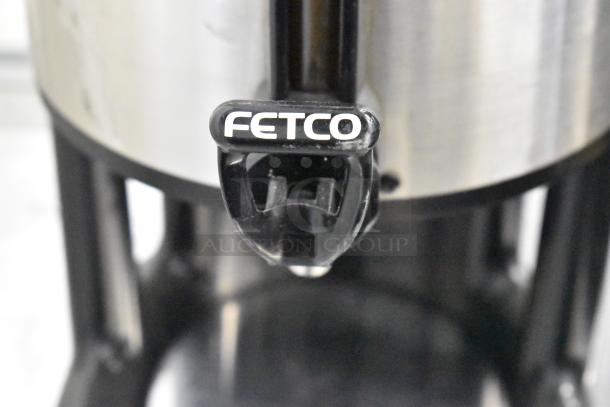 Stainless steel beverage dispenser with Fetco logo, black handle, clean surface, durable construction.