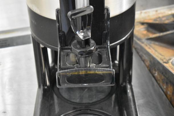 Stainless steel beverage holder dispenser with black base, featuring a push lever. Clean and well-maintained condition.