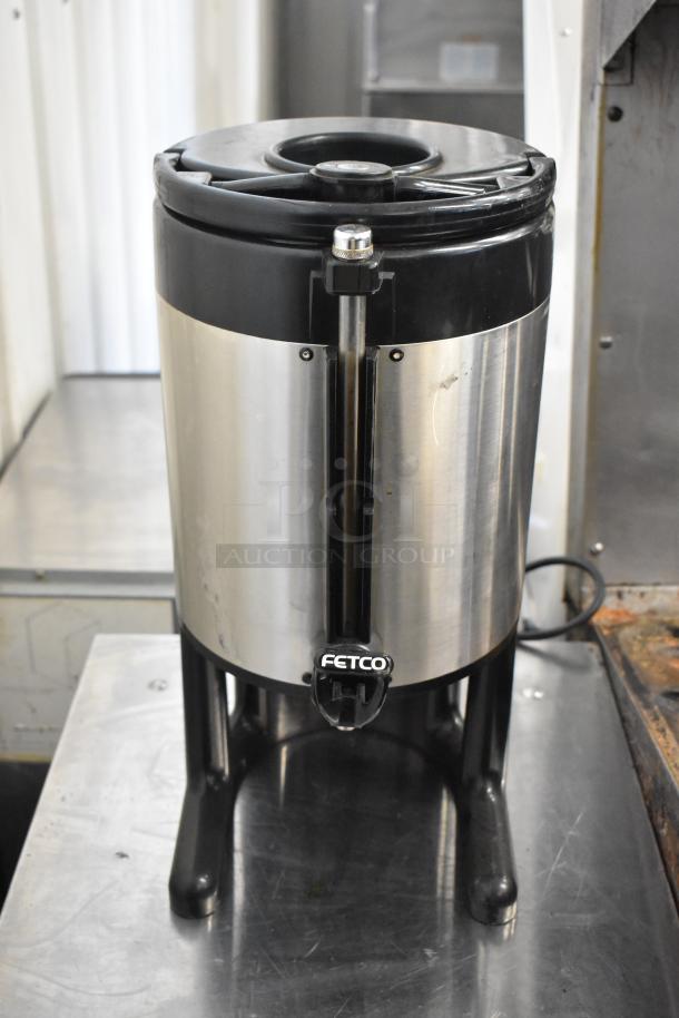 Stainless steel beverage dispenser by Fetco. Black top, sturdy legs, good condition. Ideal for commercial use.