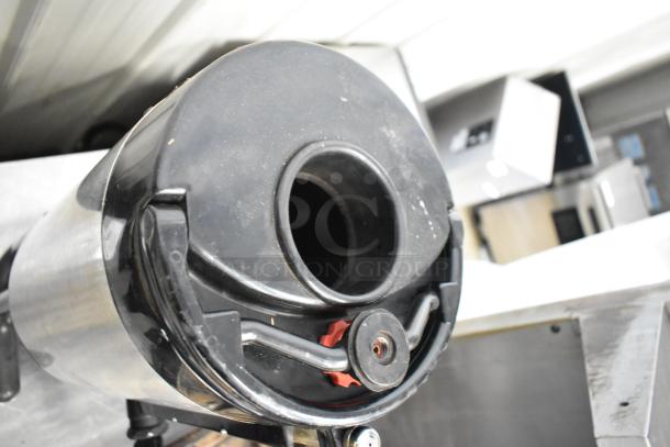 Stainless steel beverage holder dispenser with black lid, slight wear visible, features dispensing nozzle for easy use.