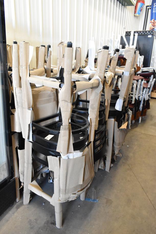 14 new Lancaster Table & Seating 164BLADBLKFR black ladder back bar height chairs, shown with protective wrapping.