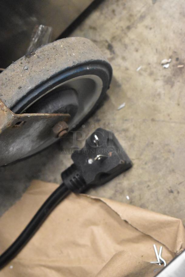 Stainless steel, dual non-stick crepe maker power plug and caster wheel on a concrete floor.
