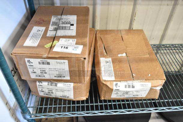 3 sealed boxes of Zebra labels, each containing 6 rolls of 1,240 labels, on a metal shelf. Labels visible on boxes.