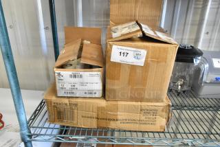 Three boxes containing 6 rolls of 1,240 Zebra labels, 164CUSHWDBLK cushions, and a phone set on a storage rack. Labels on boxes indicate product details and auction lot number. Boxes show wear.