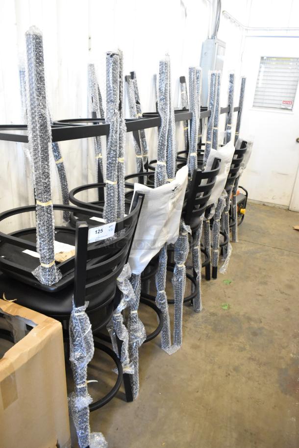 12 new Lancaster Table & Seating black ladder back bar chairs with black seat cushions, partially wrapped in bubble wrap.