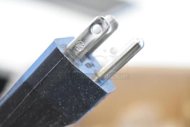 Close-up of a power plug for the Marset A654-012 Santorini Light Fixture in original box, showcasing prongs and markings.